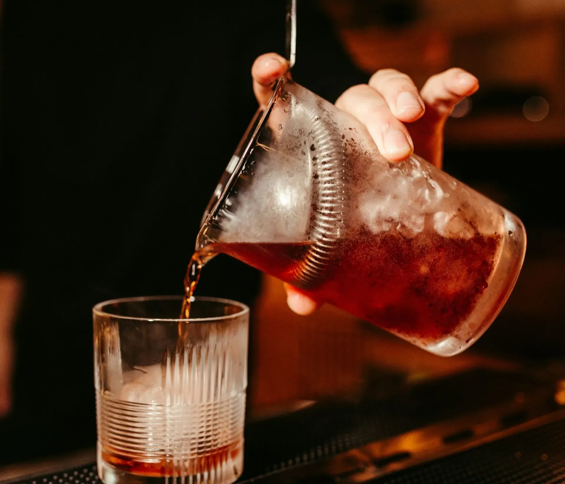 Bartender pouring a cocktail from his shaker into a glass with ice.