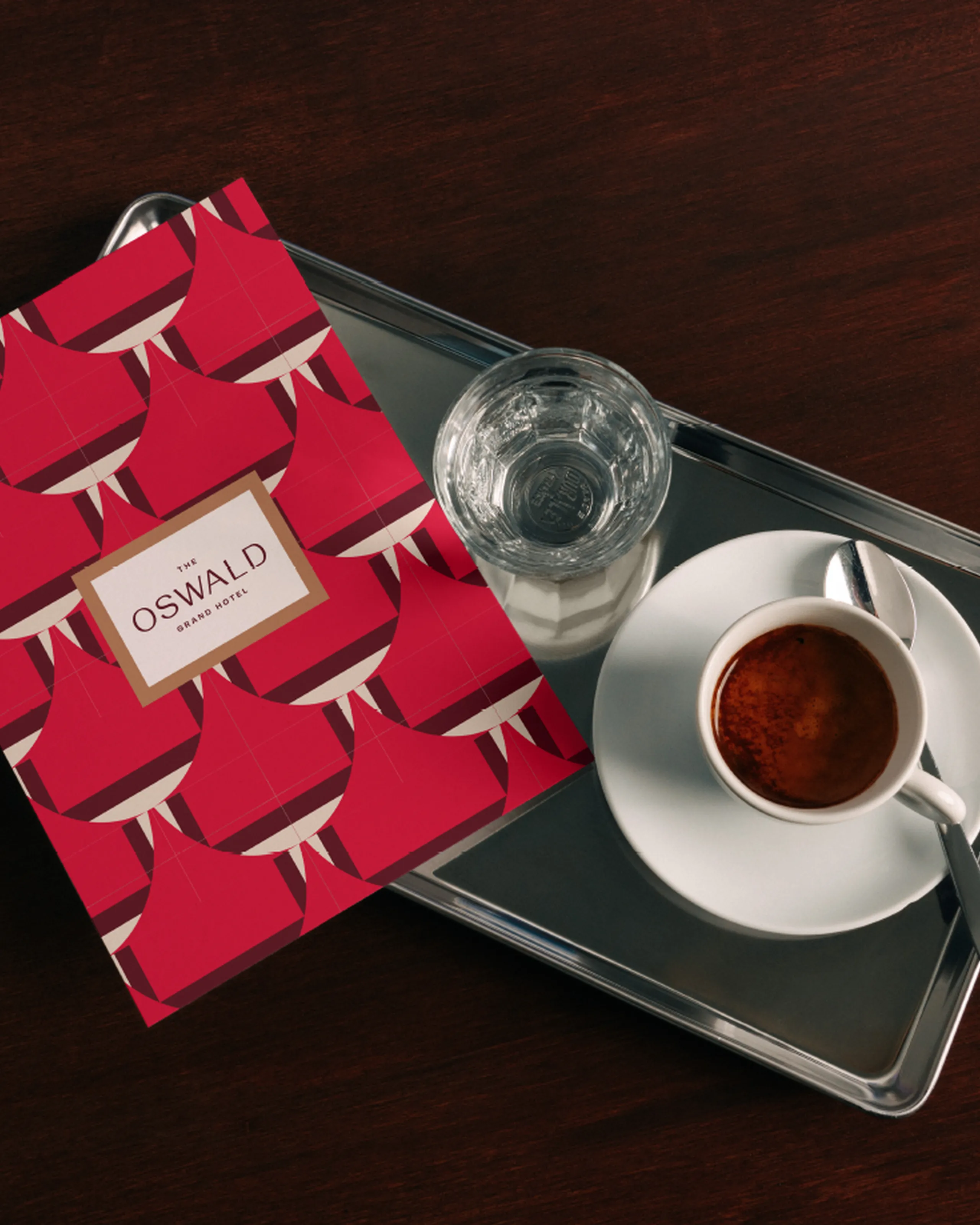 Coffee cup on a silver tray atop a mahogany table, next to a glass of water and the Hotel Oswald drinks menu.