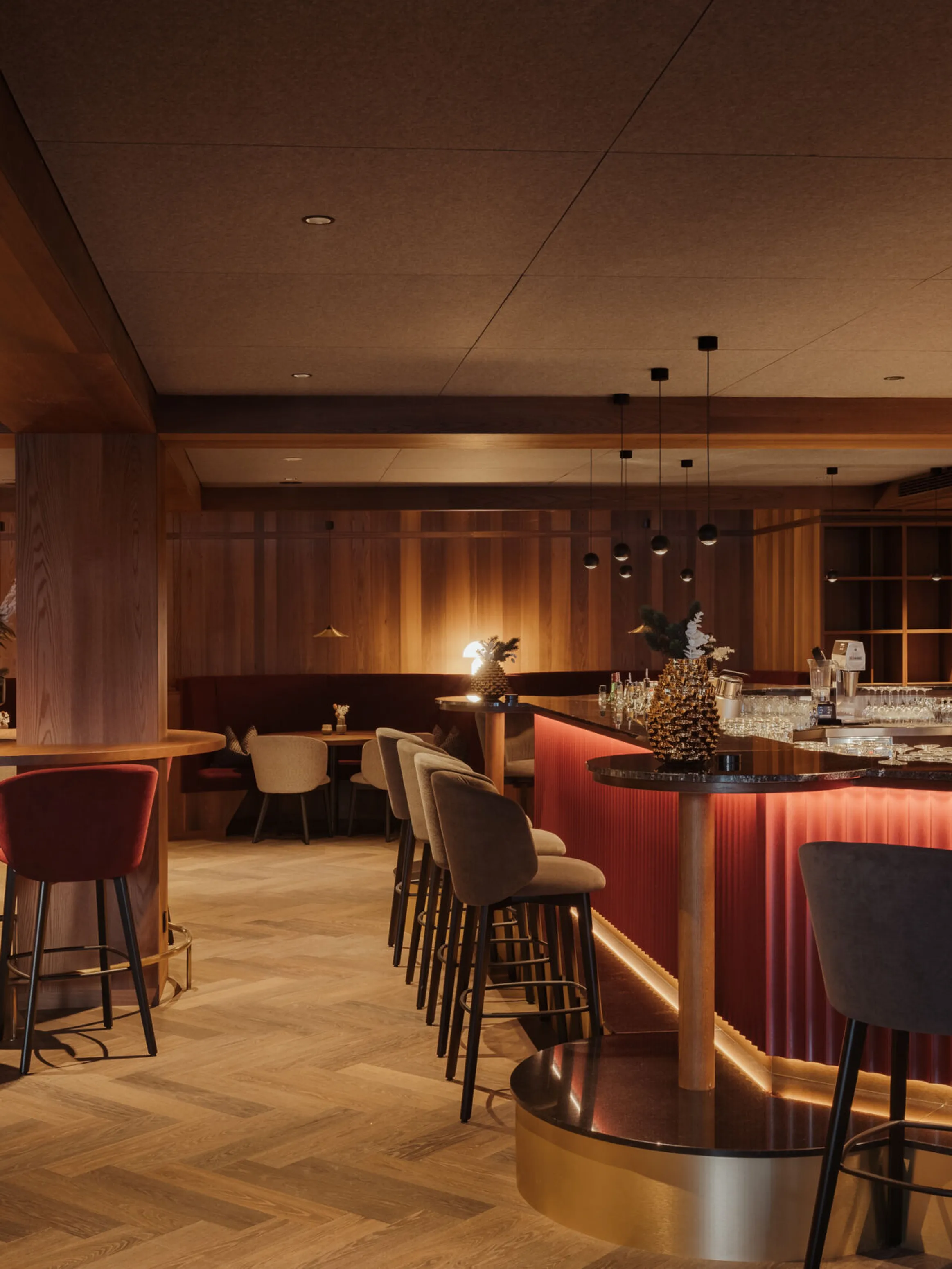 Sophisticated bar interior with a warm, ambient glow. Features a curved bar lined with plush stools, elegant wooden decor, and soft, intimate lighting.