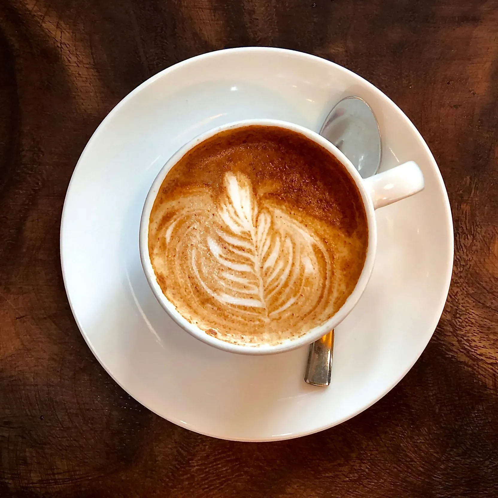 Cappuccino seen from above on a wooden table, with a leaf-shaped design in the foam.