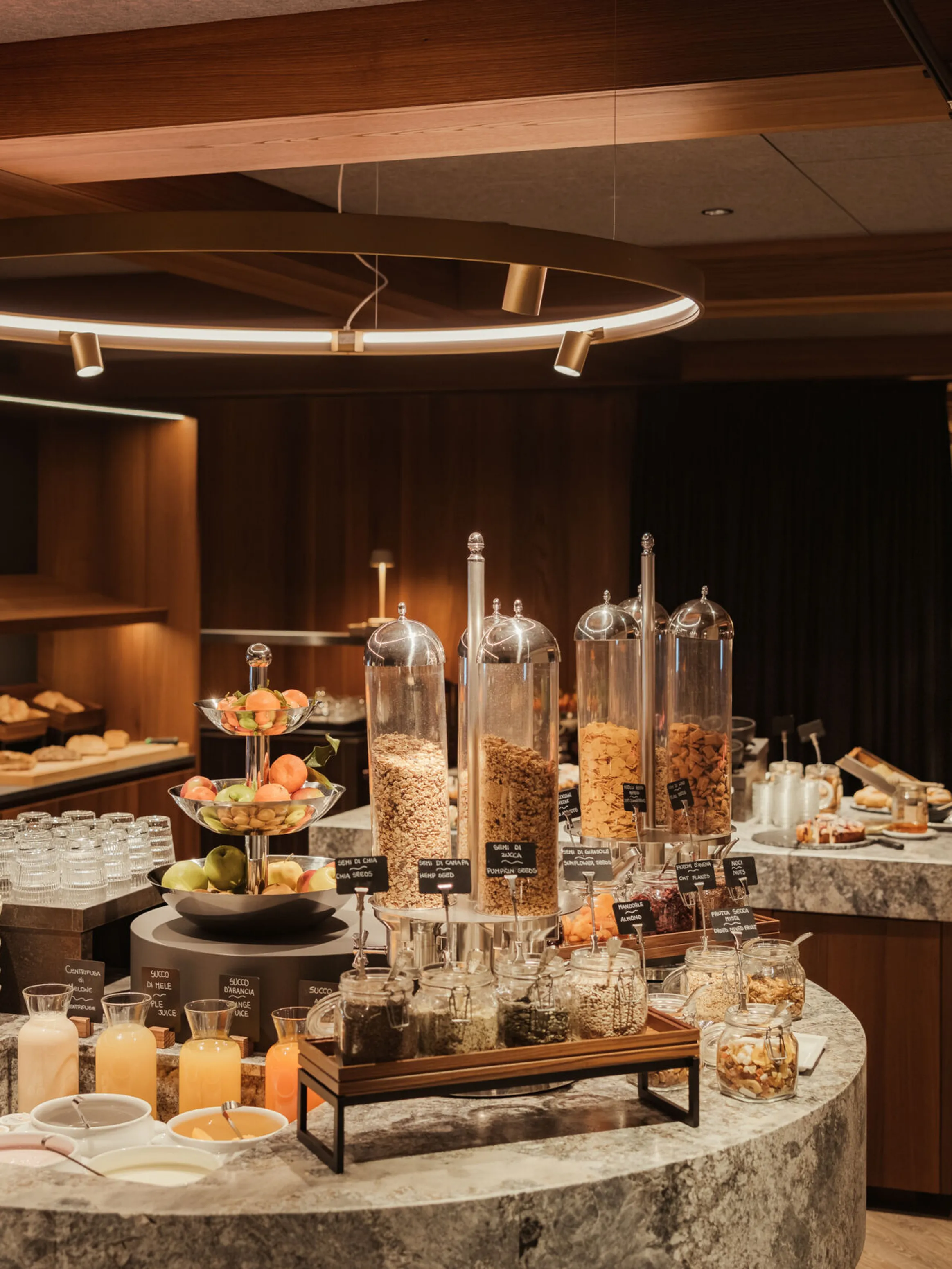 Luxurious breakfast buffet with a variety of cereals in tall dispensers, fresh fruits, pastries, juices, and cozy seating area. Warm, inviting ambiance.