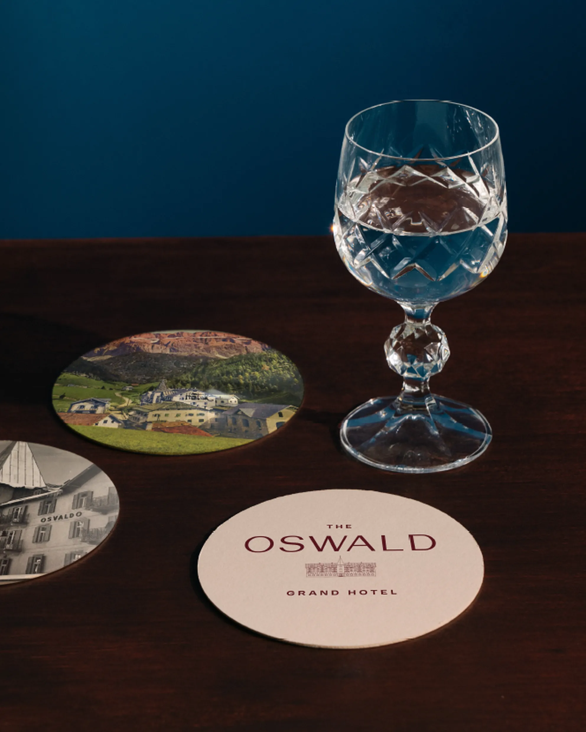 Series of Hotel Oswald coasters placed next to a crystal glass filled with water, resting on a mahogany counter.
