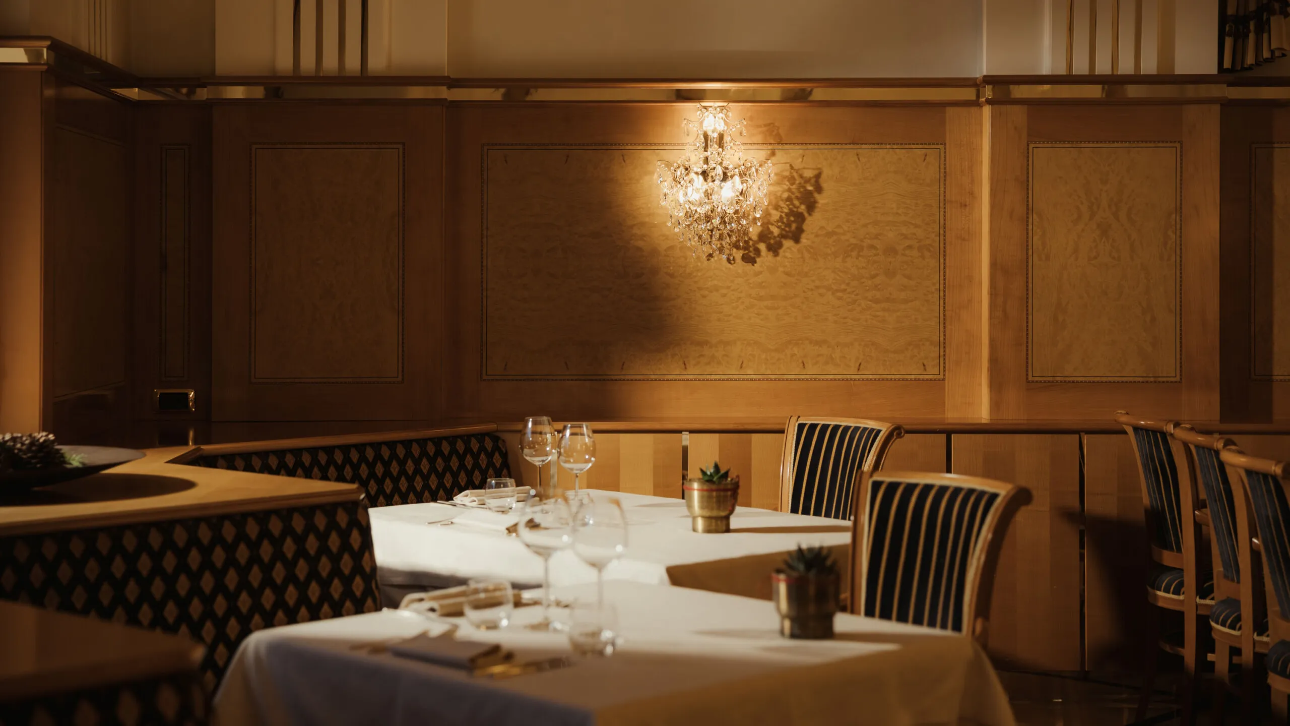 Ristorante elegante con illuminazione soffusa, lampadario di cristallo, pannelli in legno e tavoli apparecchiati con sedie a righe, creando un’atmosfera accogliente.