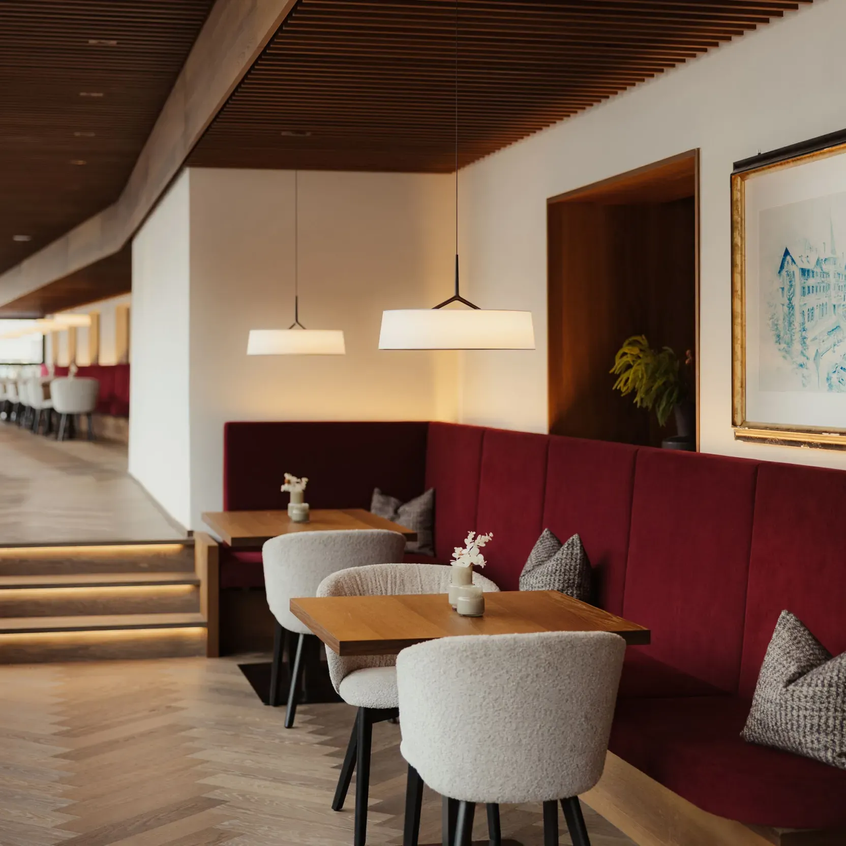Elegant restaurant interior with red velvet seating, modern wood accents, and soft lighting. Framed artwork and cozy cushions add warmth and sophistication.