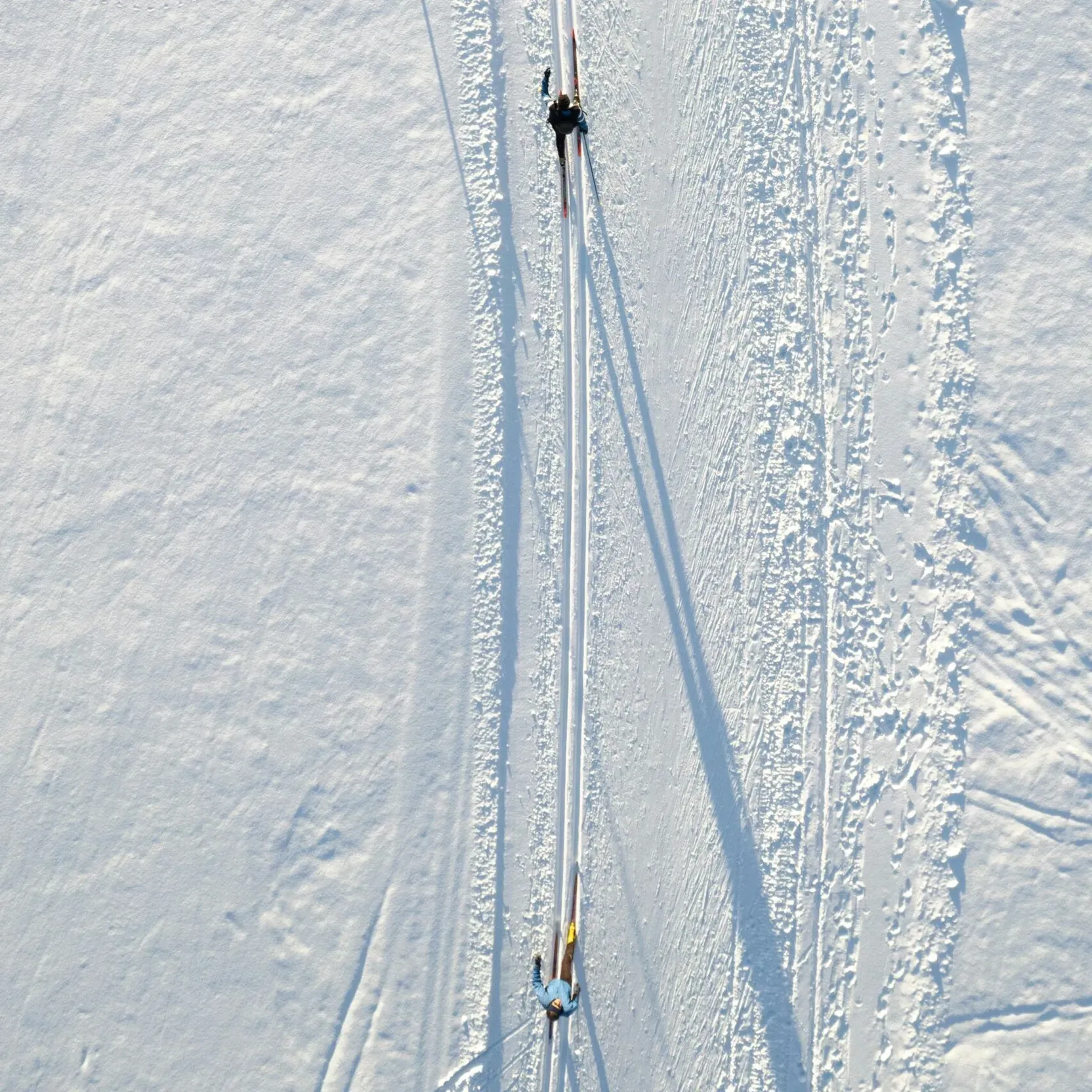 Aerial view of a cross-country ski trail with two skiers skiing along the snowy track.