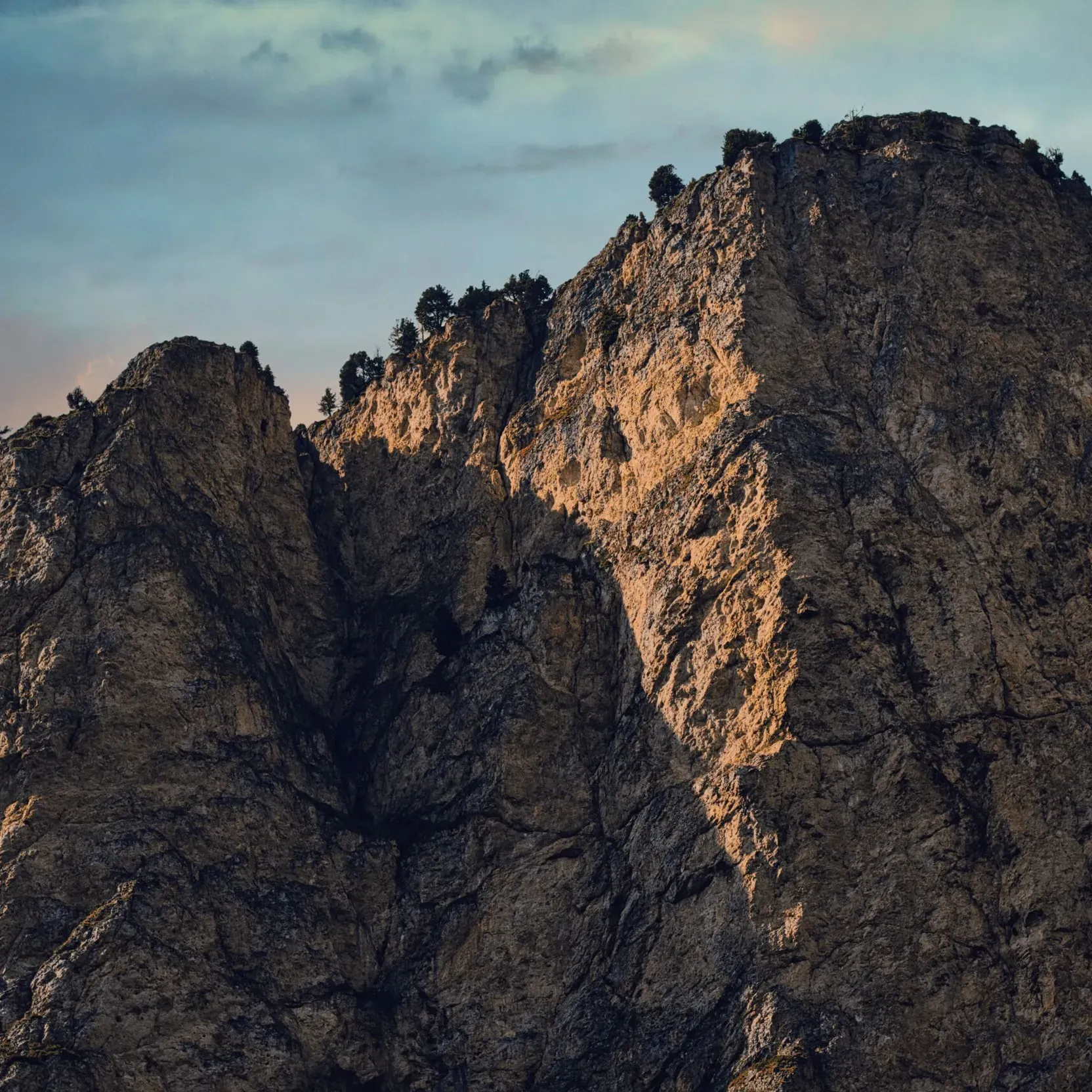 Steep, rocky mountain peak illuminated by warm light during sunset or sunrise.