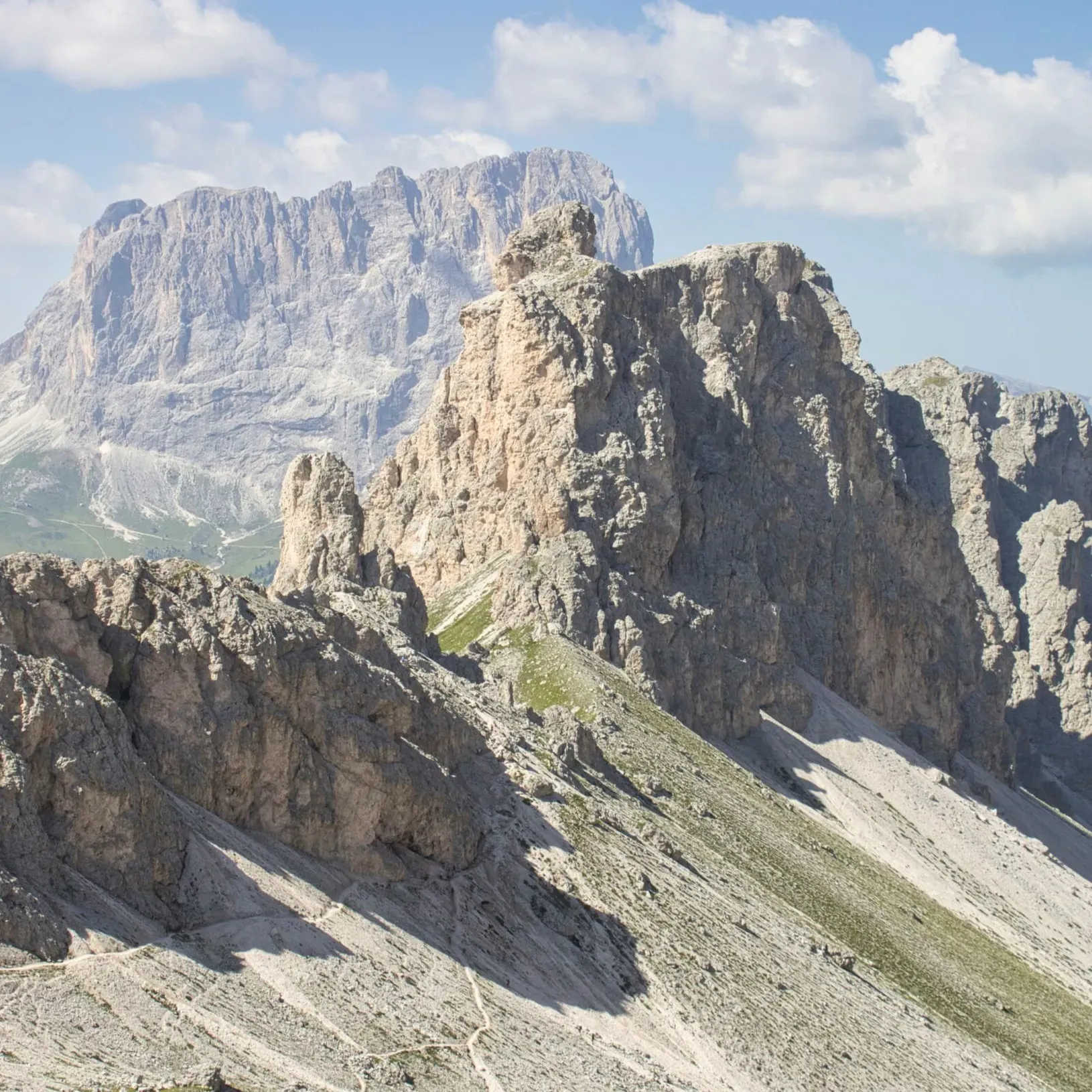 View of Forcella Cir with a trail running along the mountain ridge, and the Cir peaks and Sassolungo massif in the background.