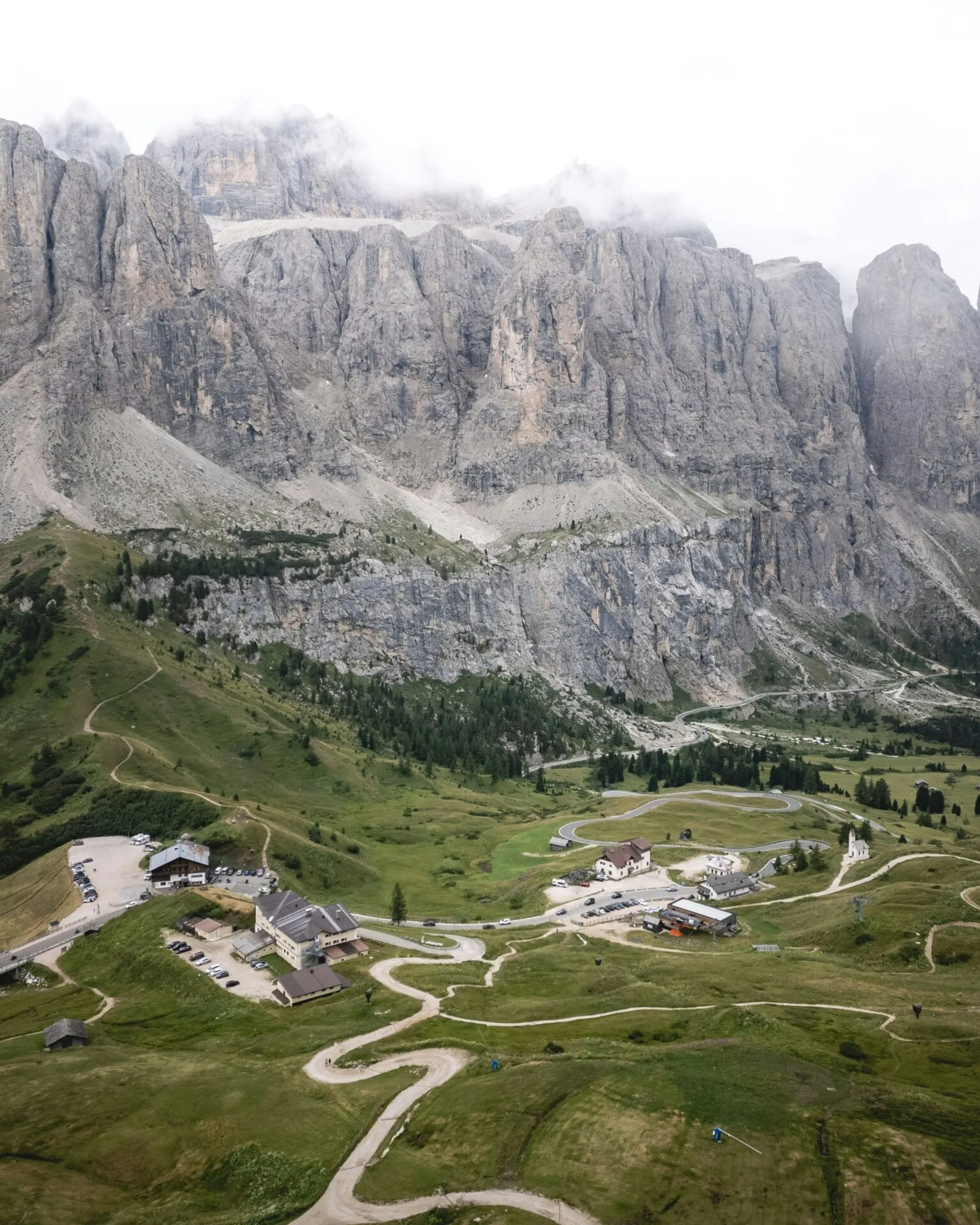 Aerial view of Passo Gardena from Forcella Cir, with the Sella massif in the background on a cloudy day.