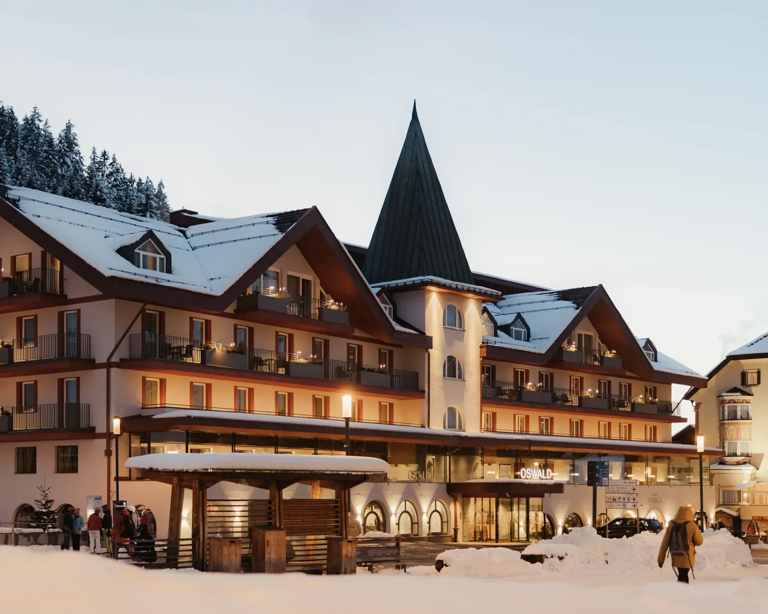 A cozy alpine hotel at dusk, surrounded by snowy landscapes and fir trees. Warm lights illuminate the building, creating a welcoming, serene atmosphere.