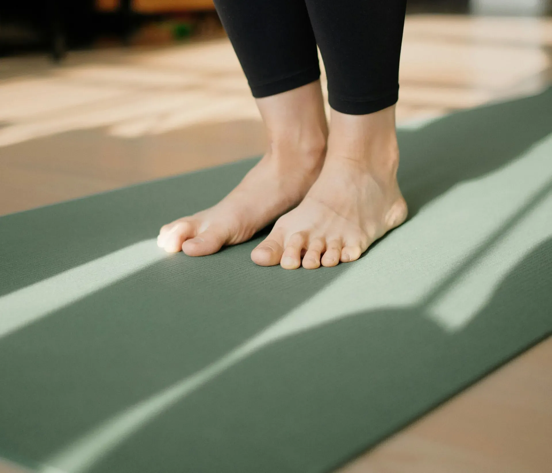 Close-up of two feet resting on a green yoga mat.