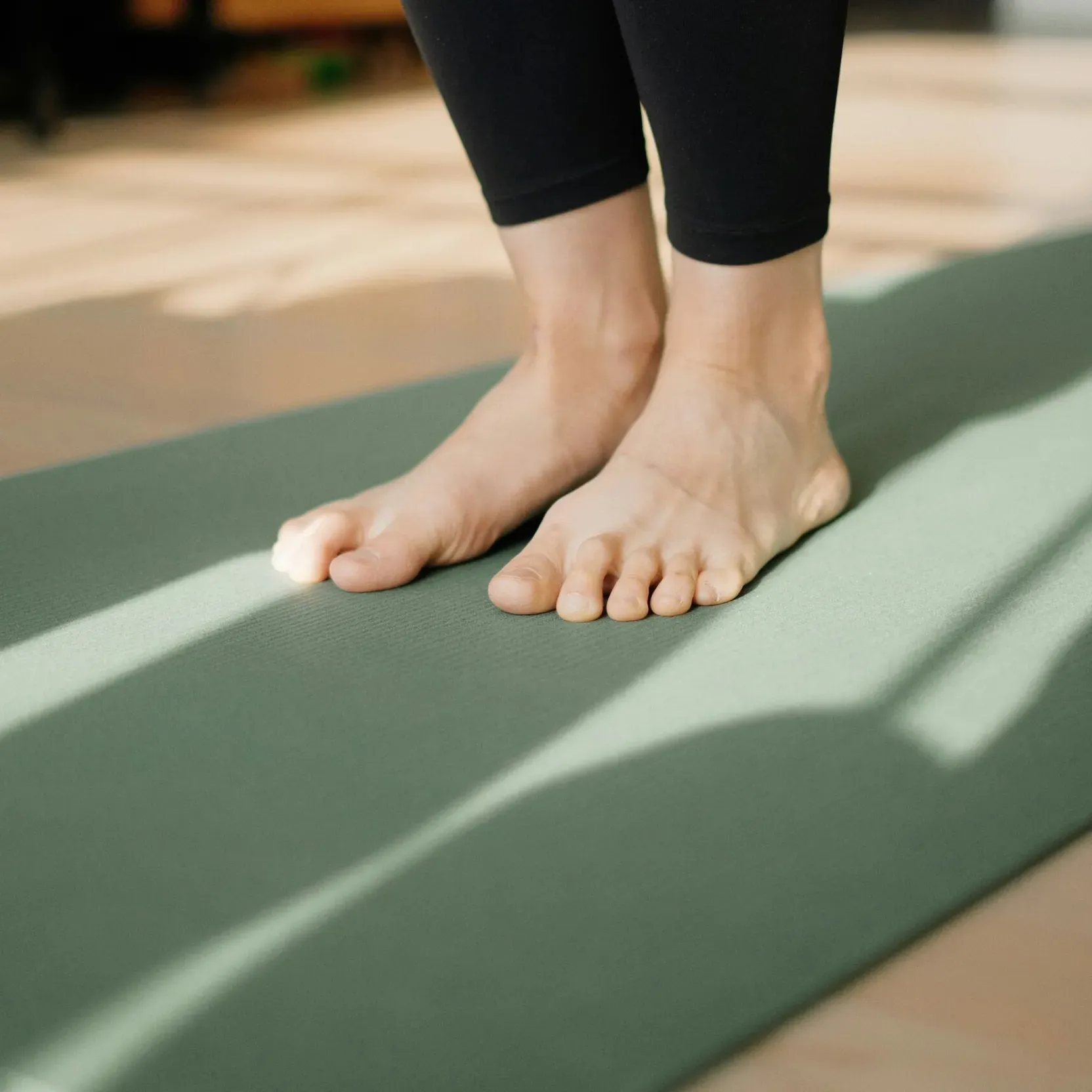 Close-up of two feet resting on a green yoga mat.