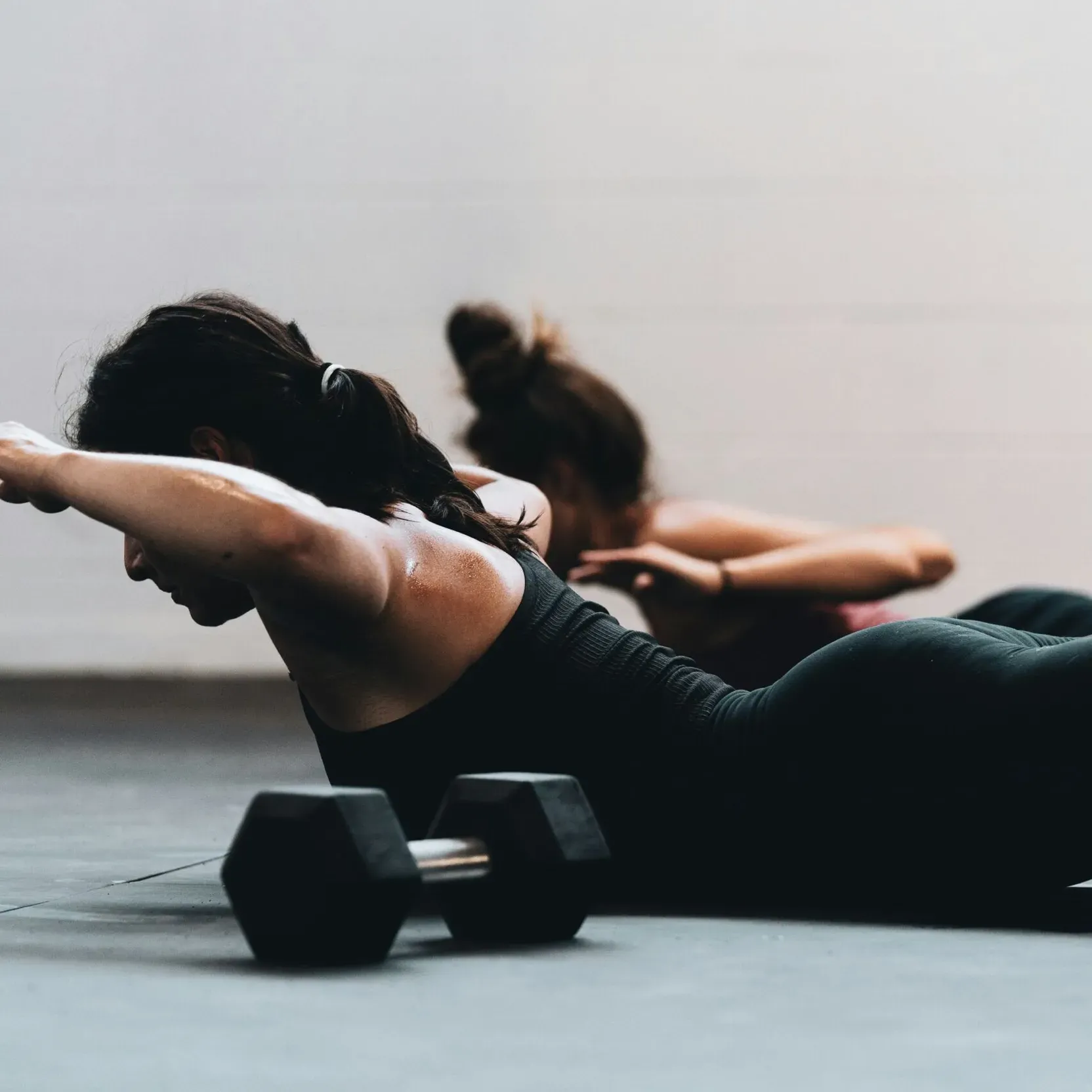 Two girls in the fitness room working their back muscles with a bodyweight exercise.