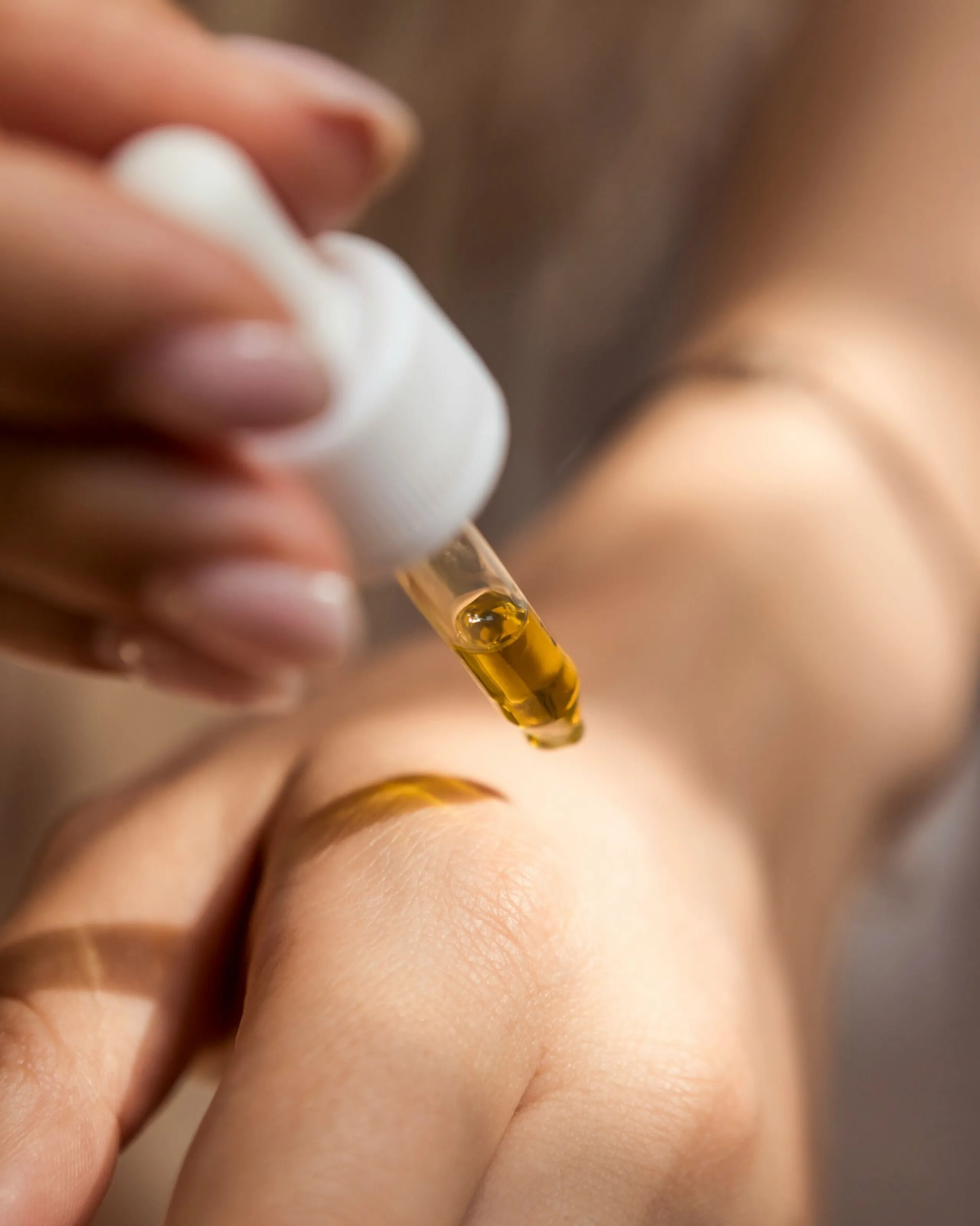 Woman’s hands holding a dropper of aromatic oil, ready to pour it onto the back of the hand.