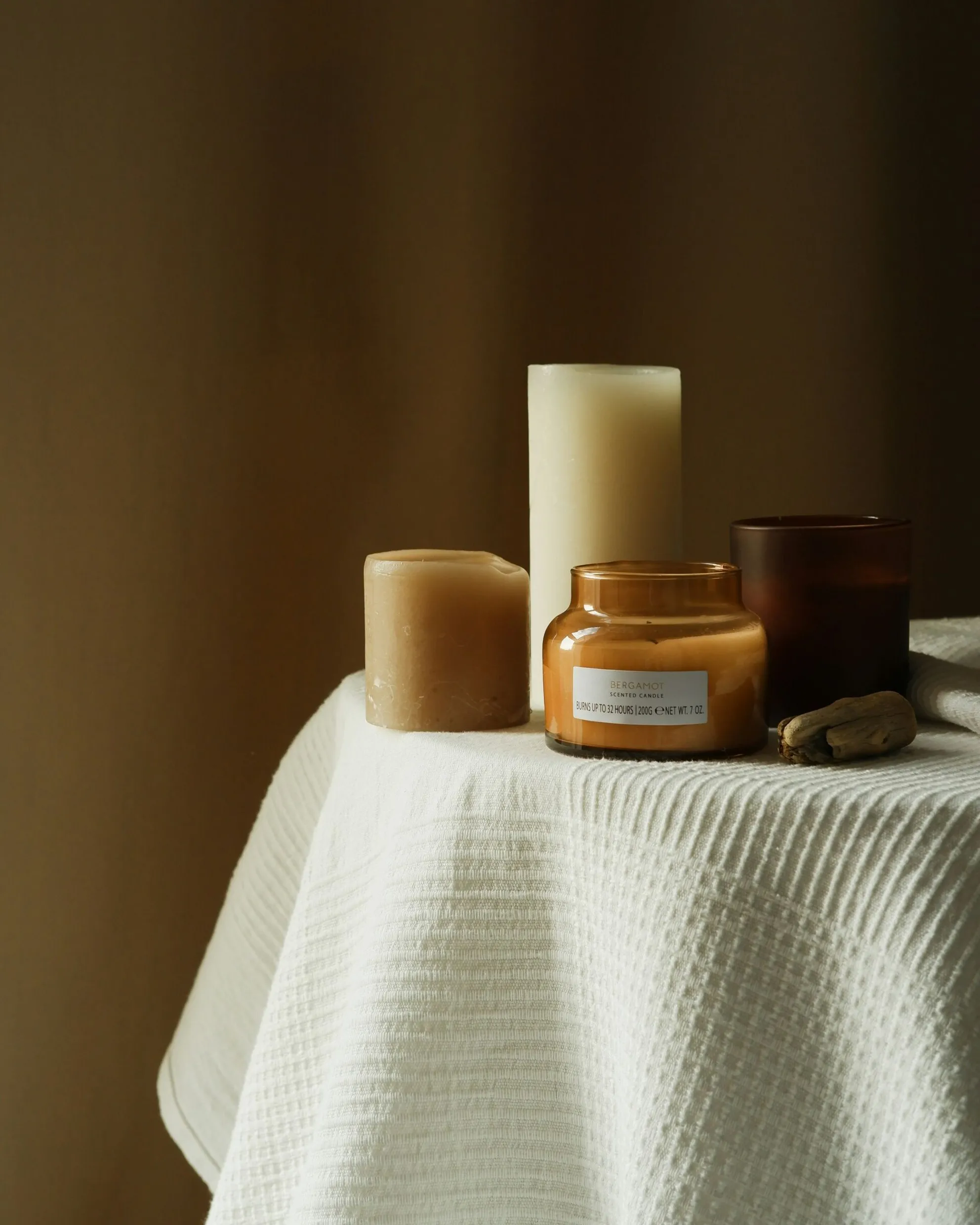 Several wax and jar candles placed on a small table with a white honeycomb-patterned tablecloth.