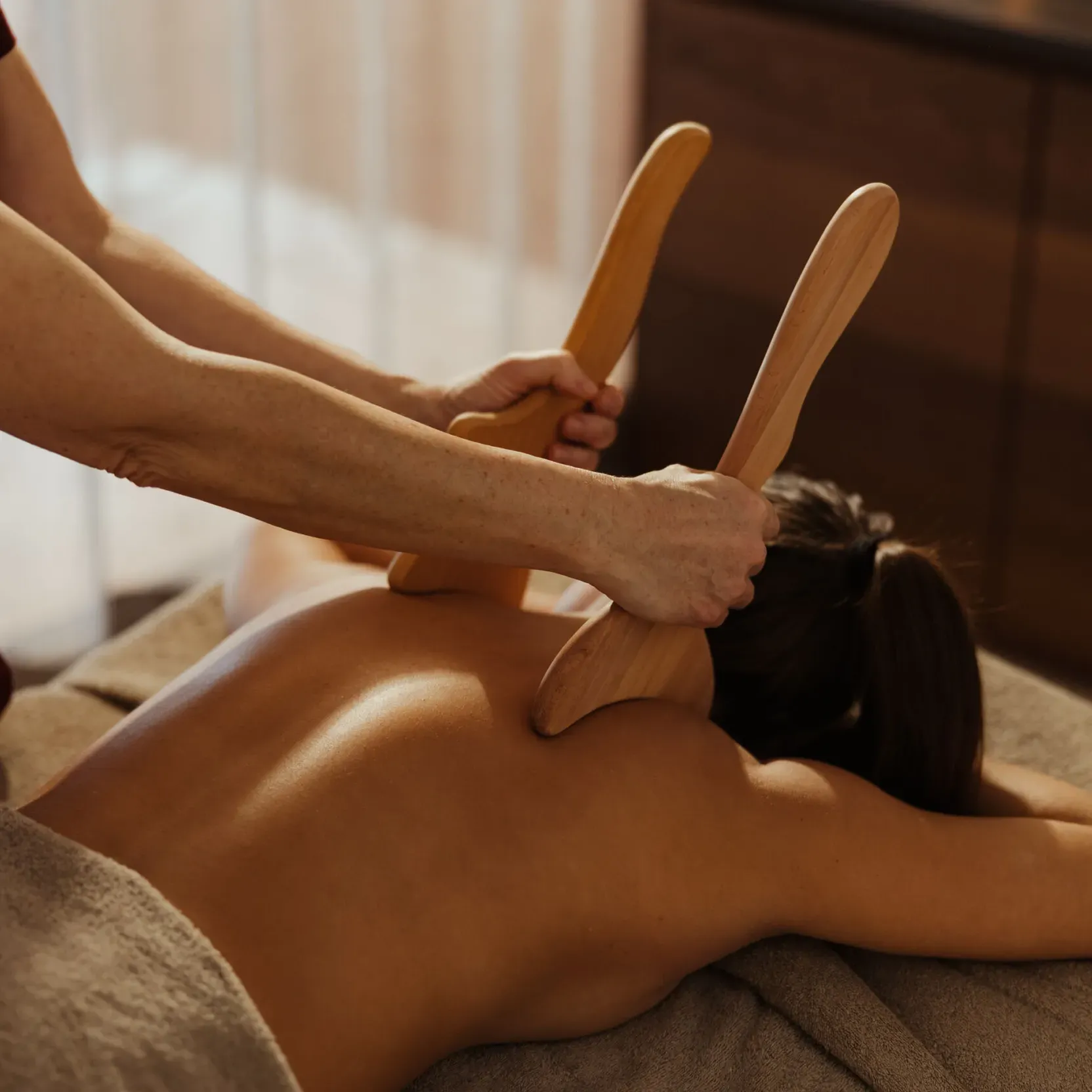 Un massaggiatore esegue un massaggio rilassante alla schiena utilizzando strumenti in legno su una persona distesa a pancia in giù, creando un’atmosfera calma e rilassante tipica di una spa.