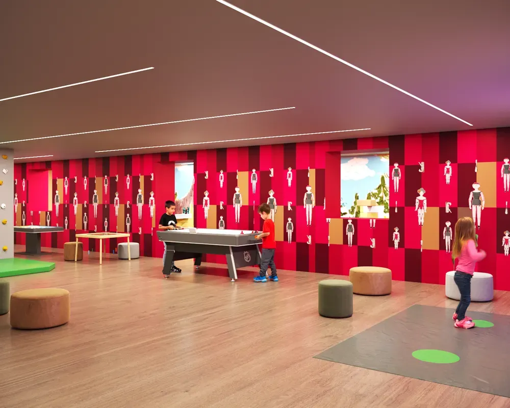 Children’s playroom with a pool table, climbing wall, and other games, featuring upholstery with the typical Hotel Oswald pattern and doll illustrations on the walls, with children playing.