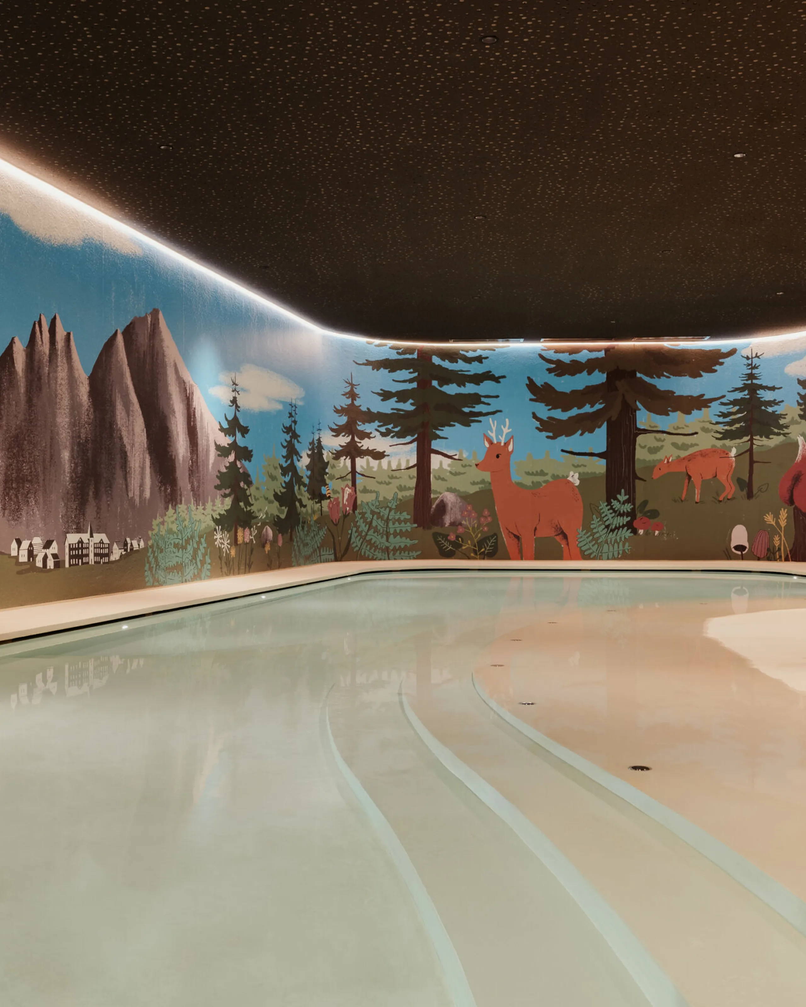 Indoor pool with gentle lighting. Walls feature a mural of mountains, trees, and animals. Playful toys like a blue dinosaur and red kangaroo surround the pool.