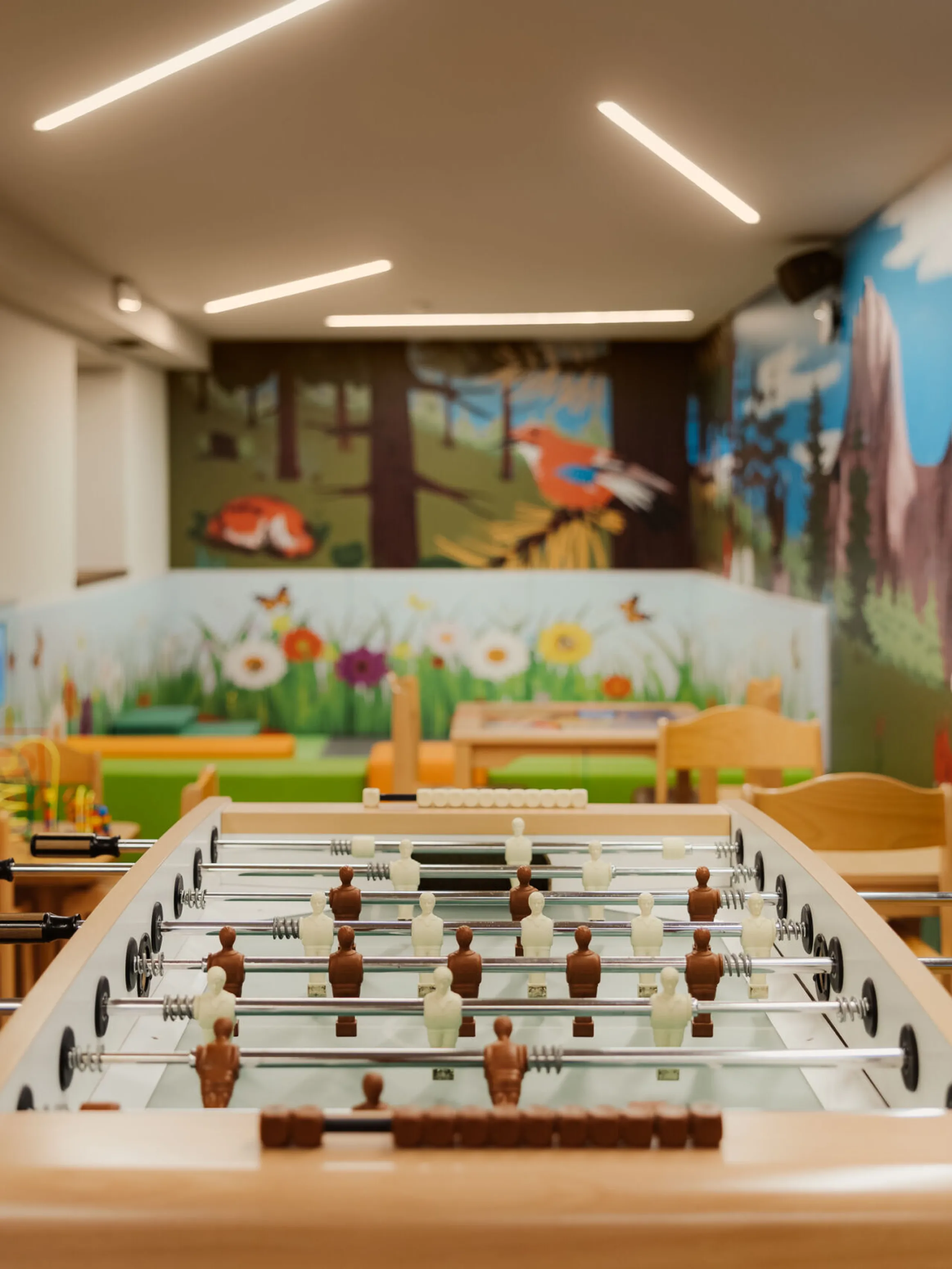 Child-friendly playroom with a foosball table and vibrant mural of mountains, trees, and animals. Cozy, inviting atmosphere with soft lighting.