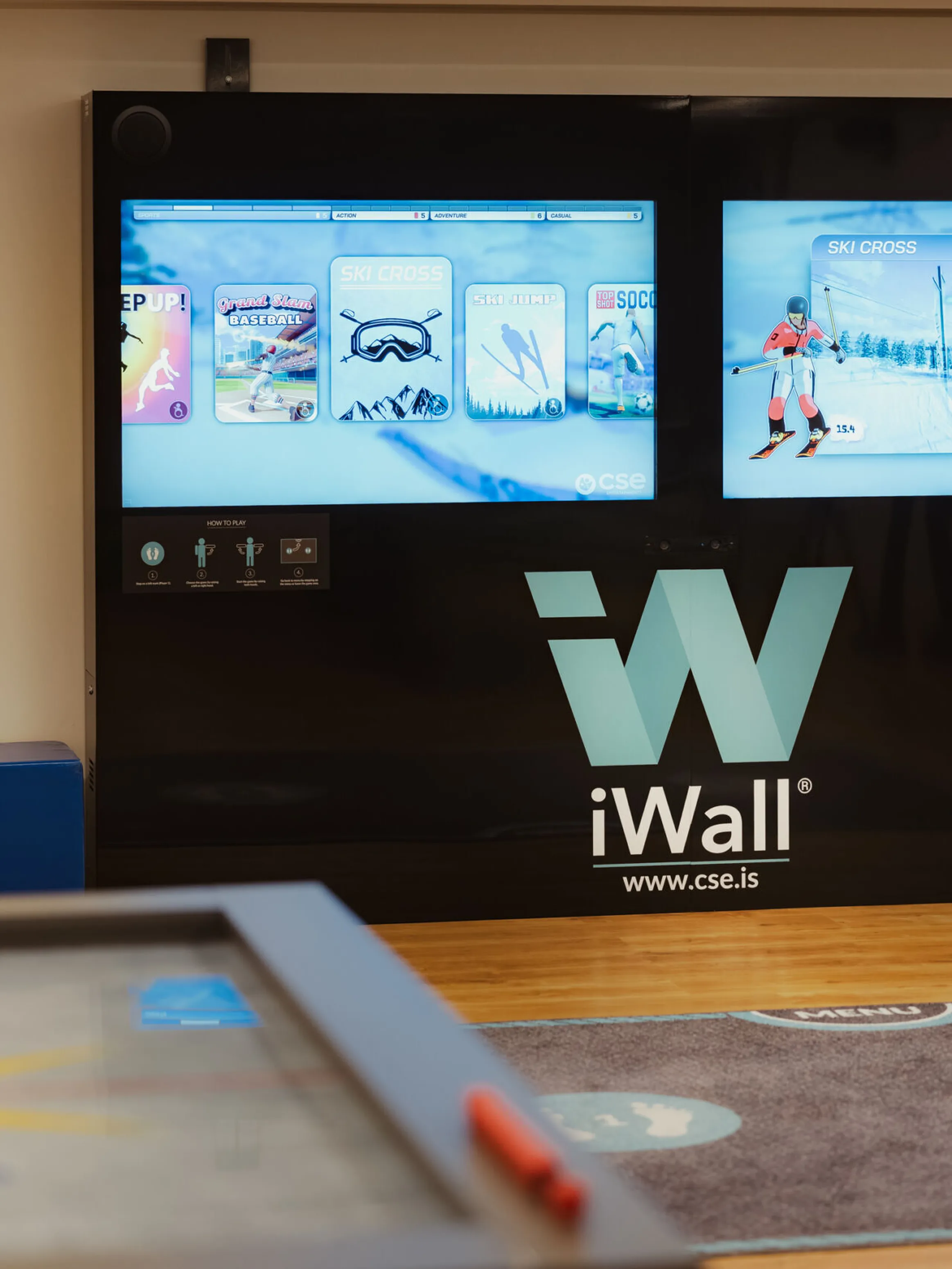 Interactive gaming setup with two digital screens displaying winter sports games, branded "iWall" on a black background. Modern and engaging atmosphere.