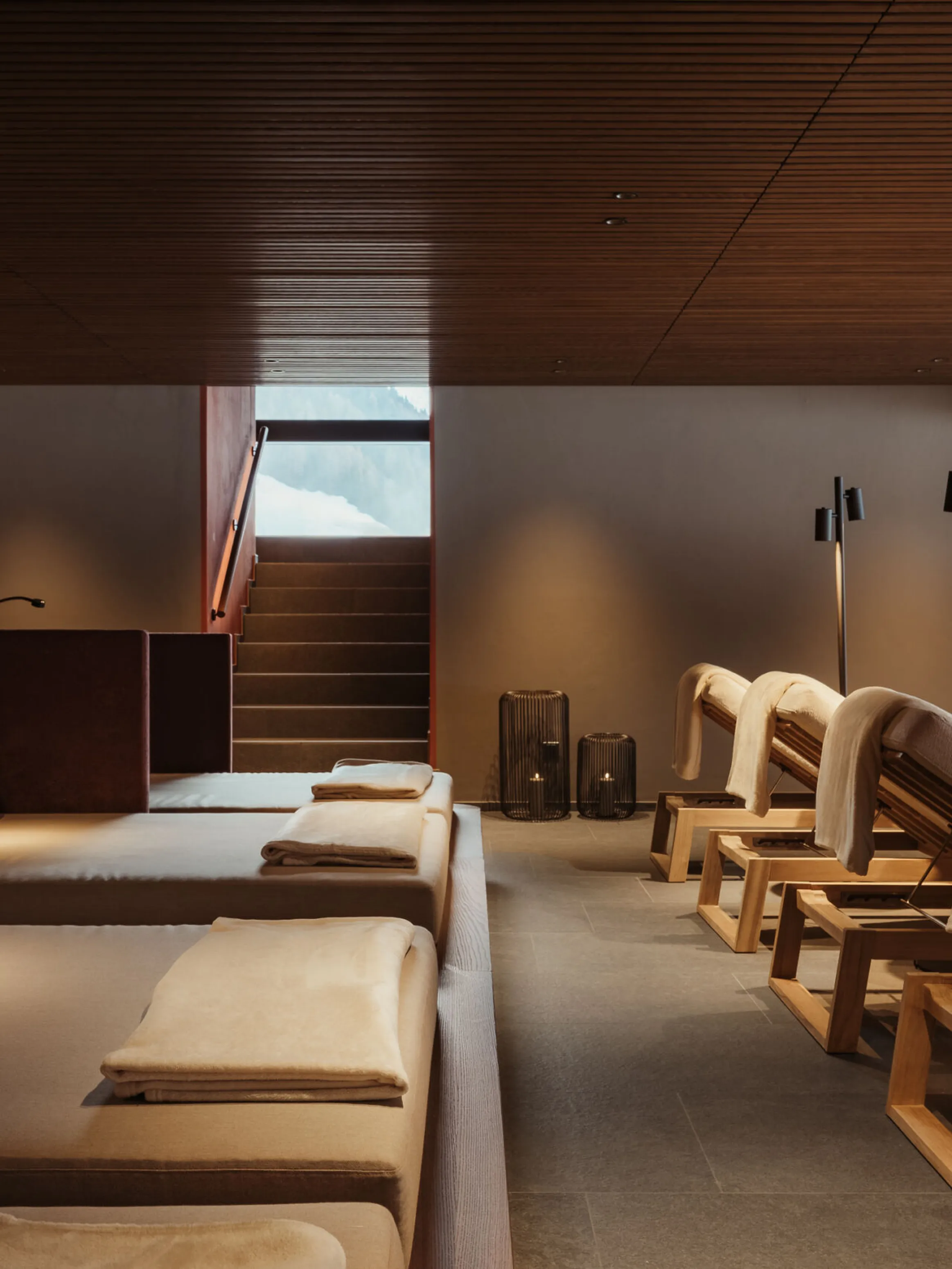 Luxurious spa room with wooden loungers, plush pillows, and soft lighting. The modern decor and earthy tones create a serene, relaxing atmosphere.