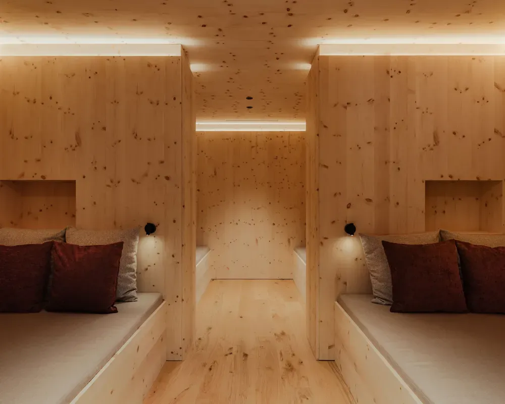 Gemütlicher Holzraum mit zwei beigen Lounge-Sesseln, jeweils mit bordeaux- und grauen Kissen dekoriert. Weiches Ambientelicht schafft eine warme und ruhige Atmosphäre.