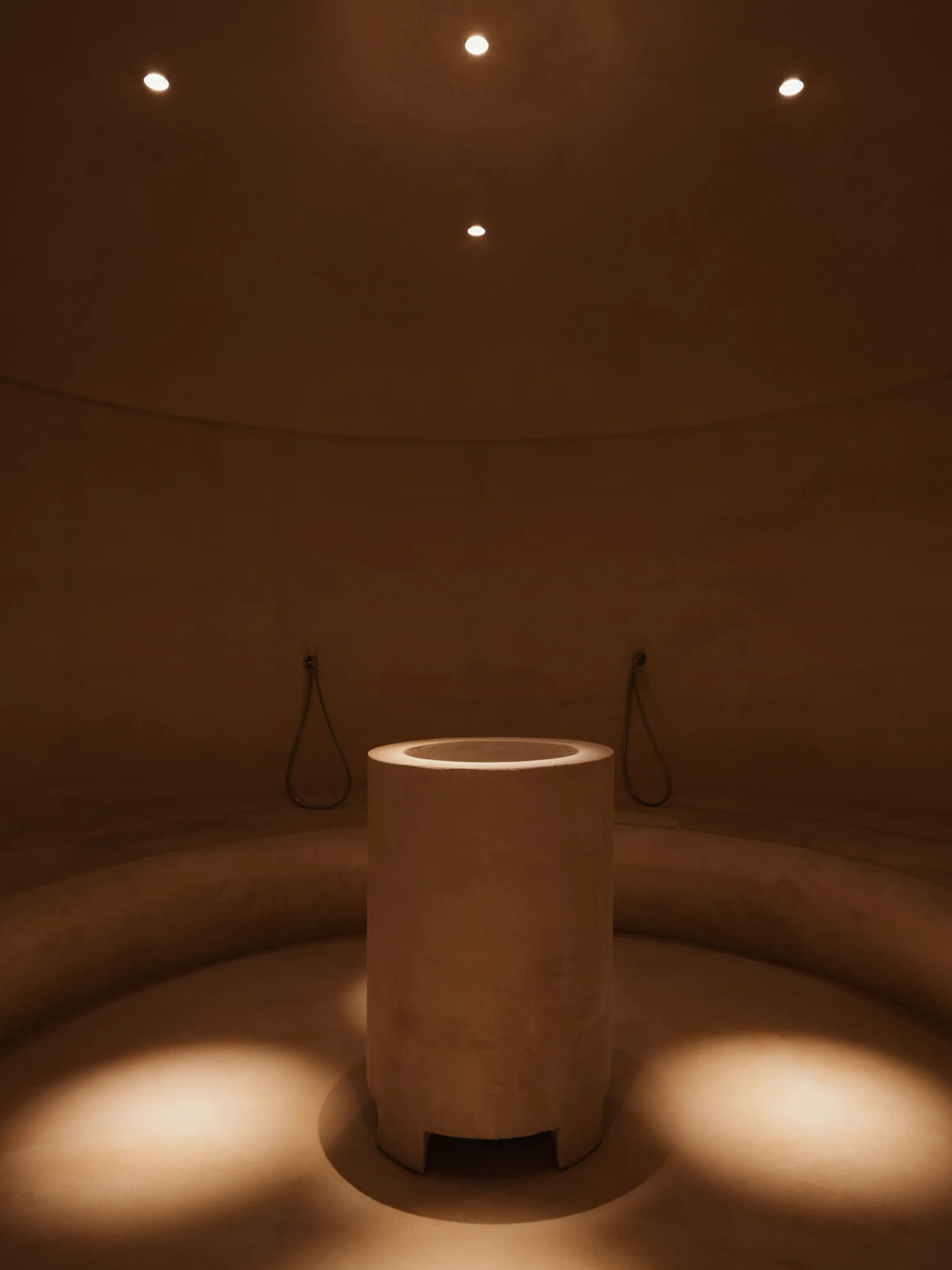 A dimly lit circular room features a central cylindrical pedestal under soft, focused lights, creating a serene, minimalist ambiance.