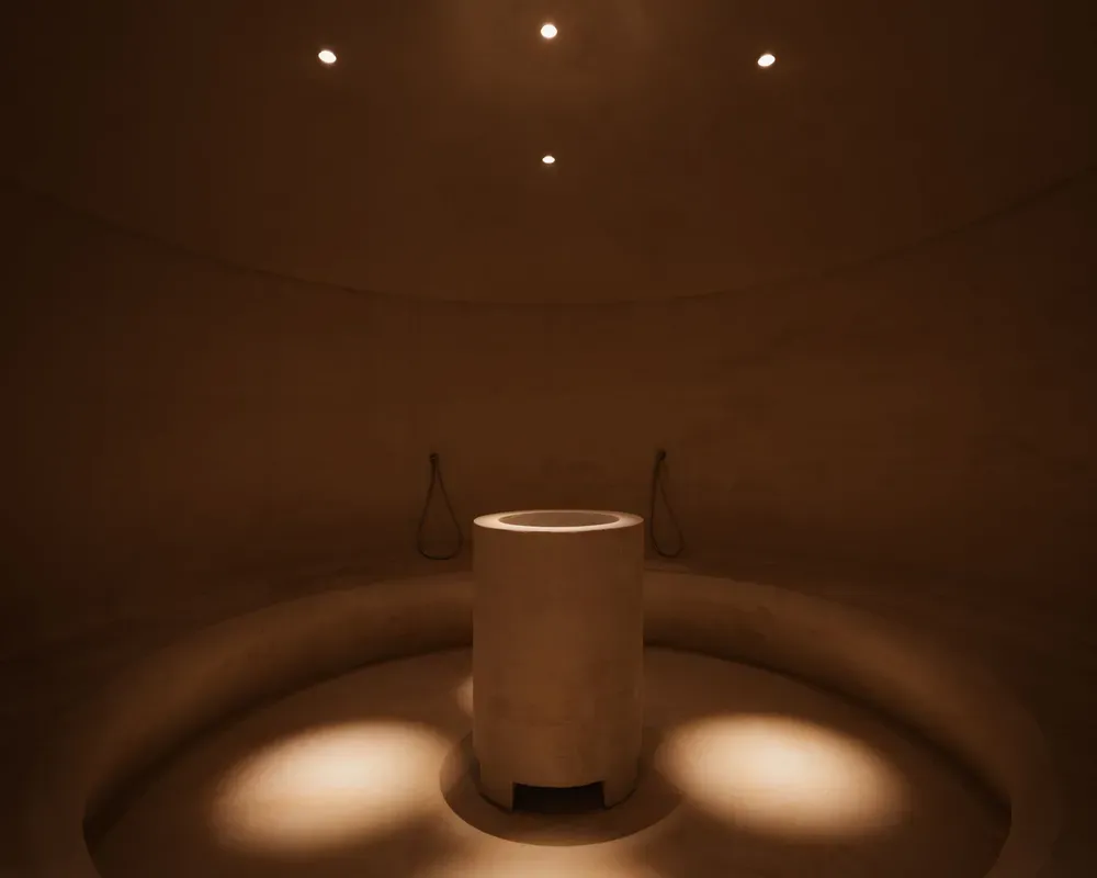 Ein schwach beleuchteter runder Raum verfügt über einen zentralen zylindrischen Sockel unter sanften, fokussierten Lichtern, die eine ruhige, minimalistische Atmosphäre schaffen.